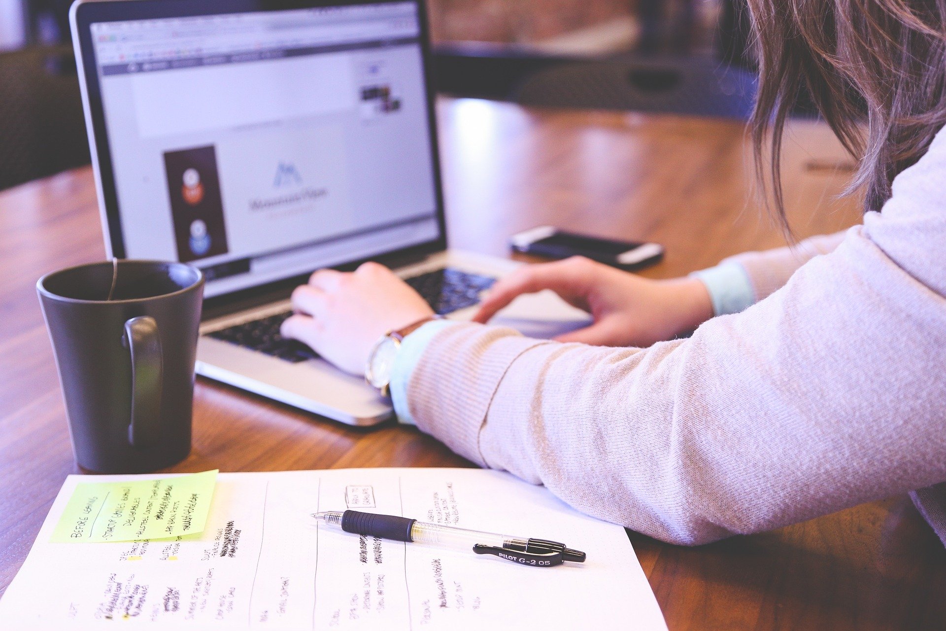 Woman typing on a laptop with a mug of tea