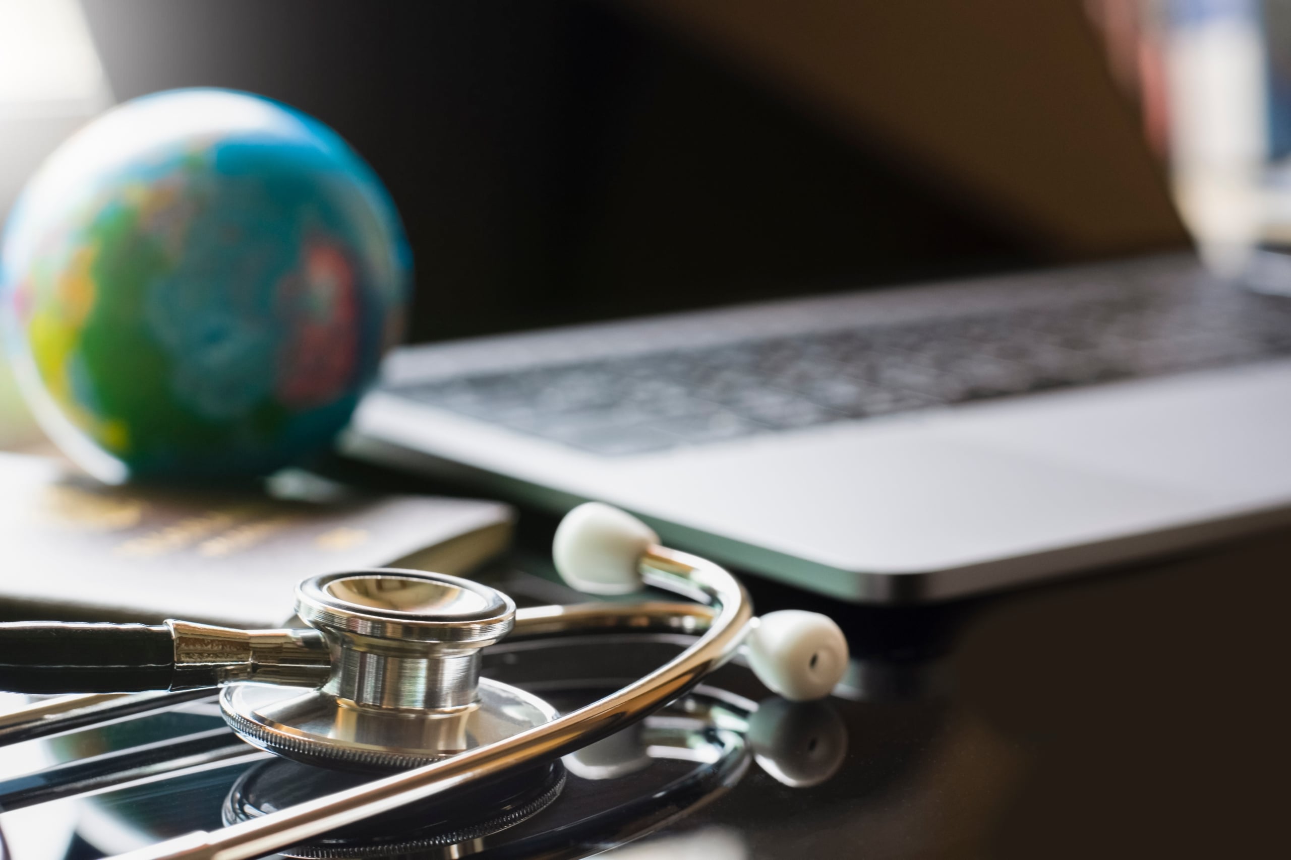 Close up of stethoscope next to laptop and globe