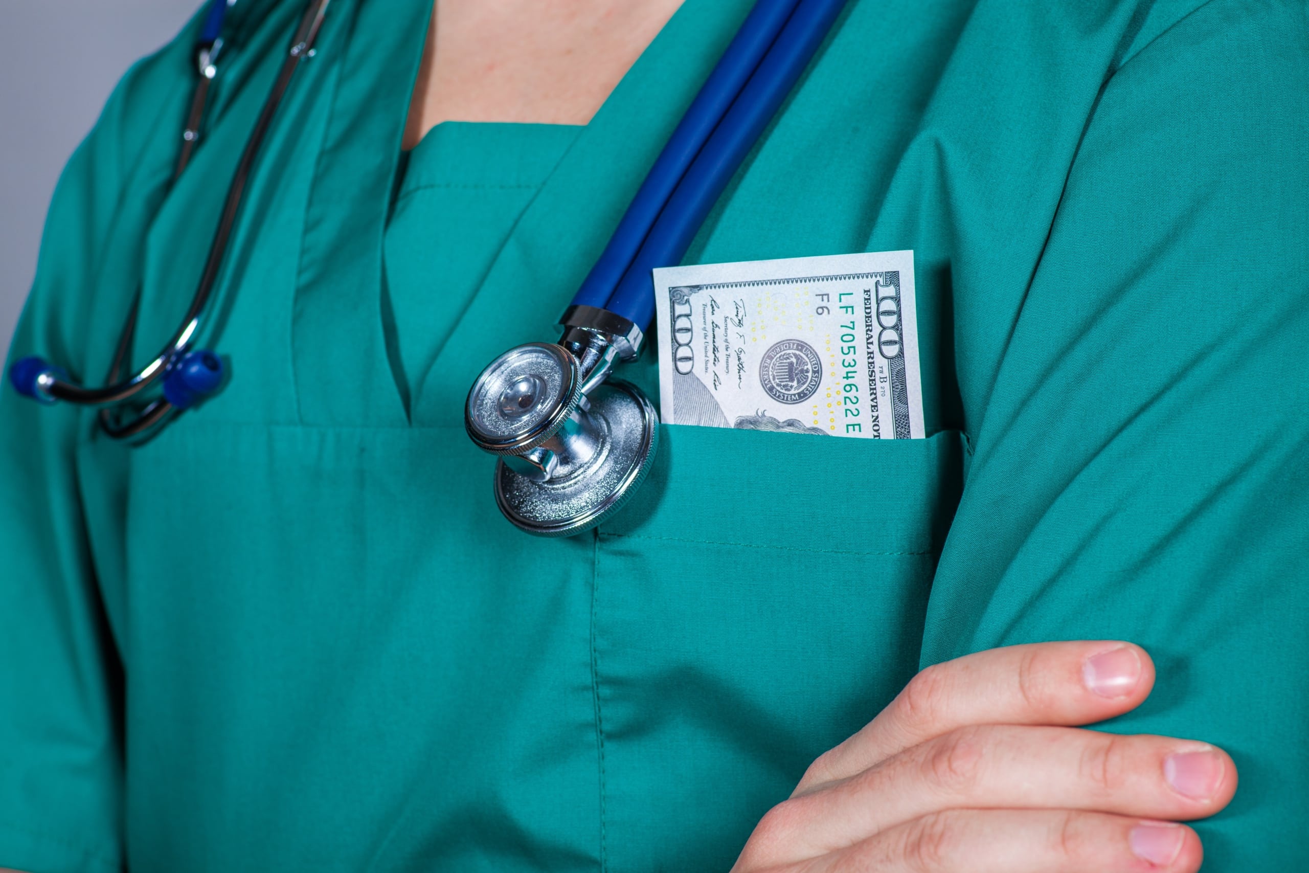 A nurse in scrubs with money in their pocket