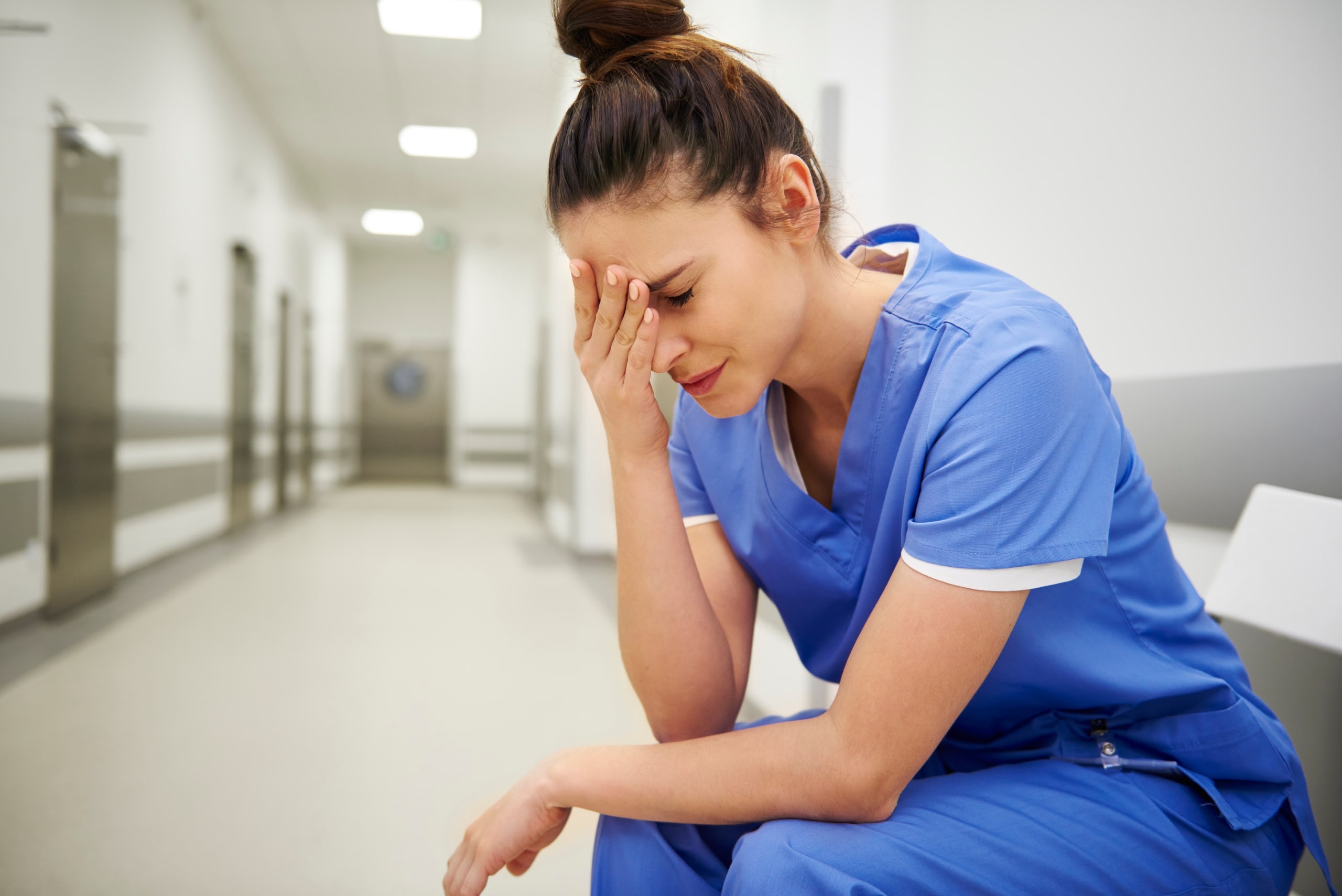 Nurse holding her head while seated in a hallway