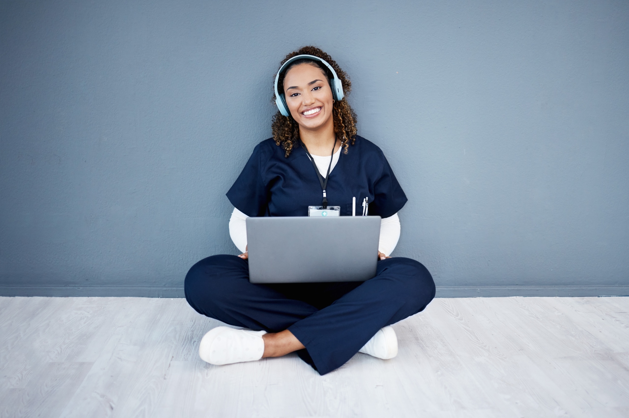 Nurse sitting on the ground while wearing headphones and using a laptop