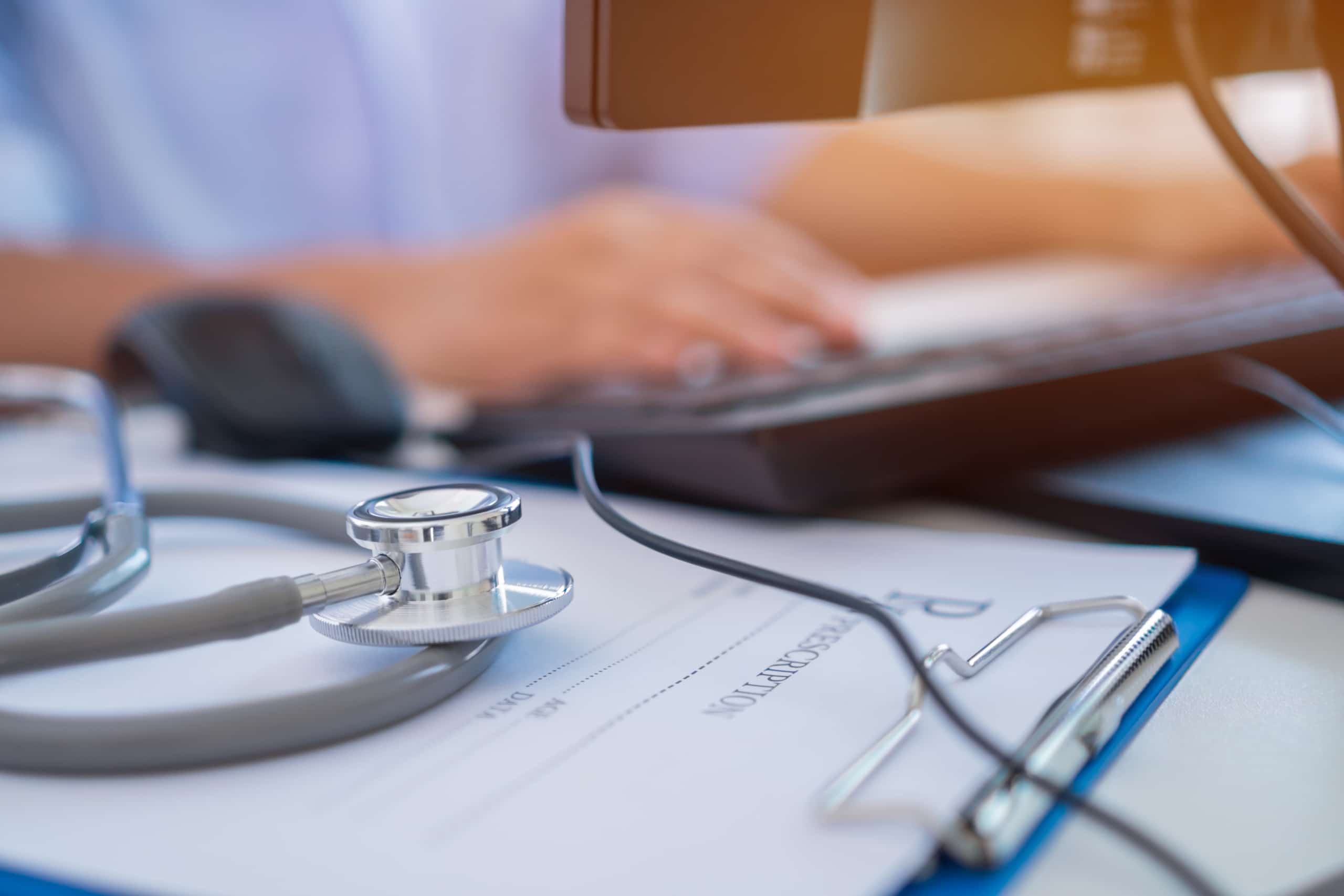 Close up of a medical professional with a stethoscope typing on a keyboard