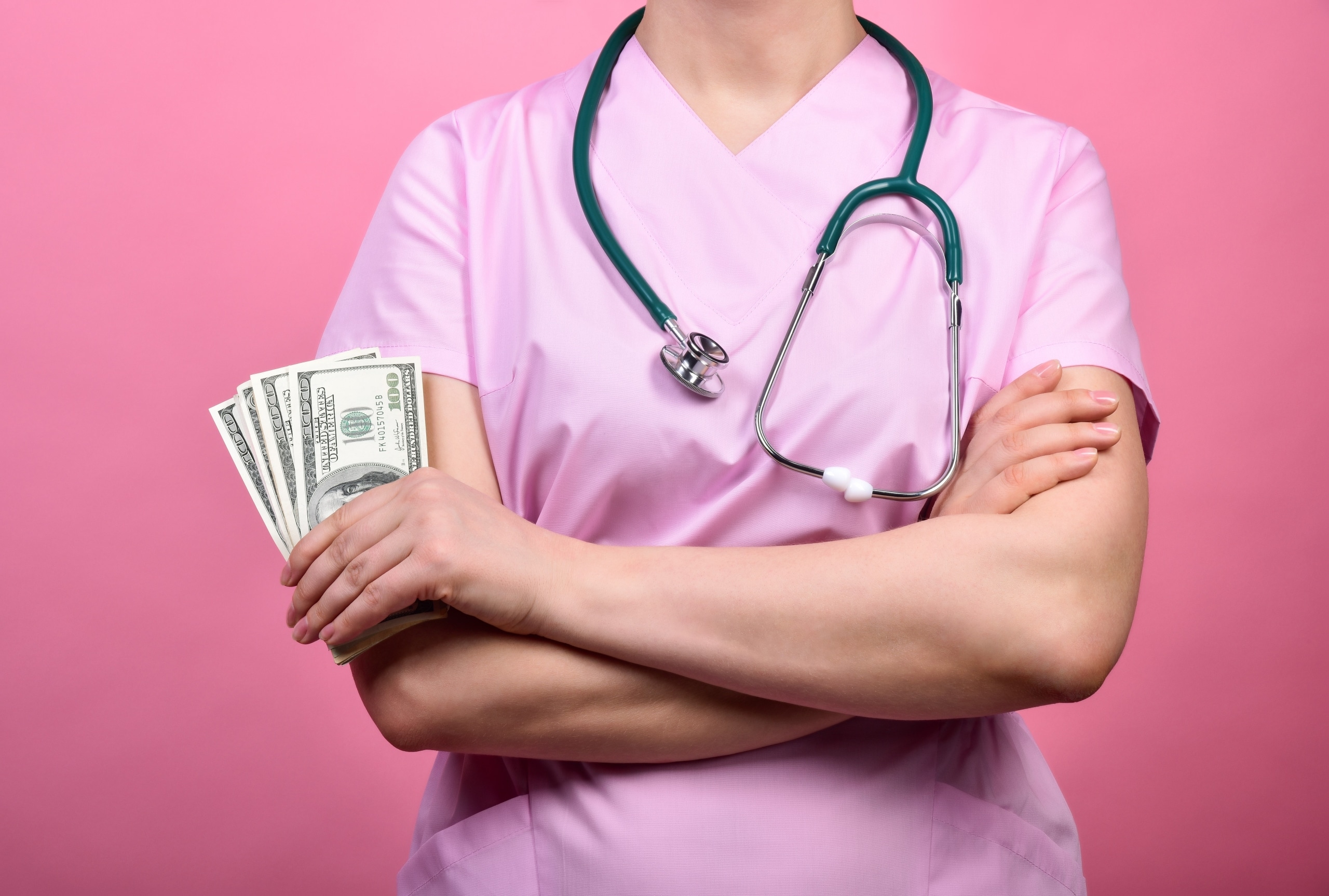 Close up of a nurse in pink scrubs holding 100 dollar bills
