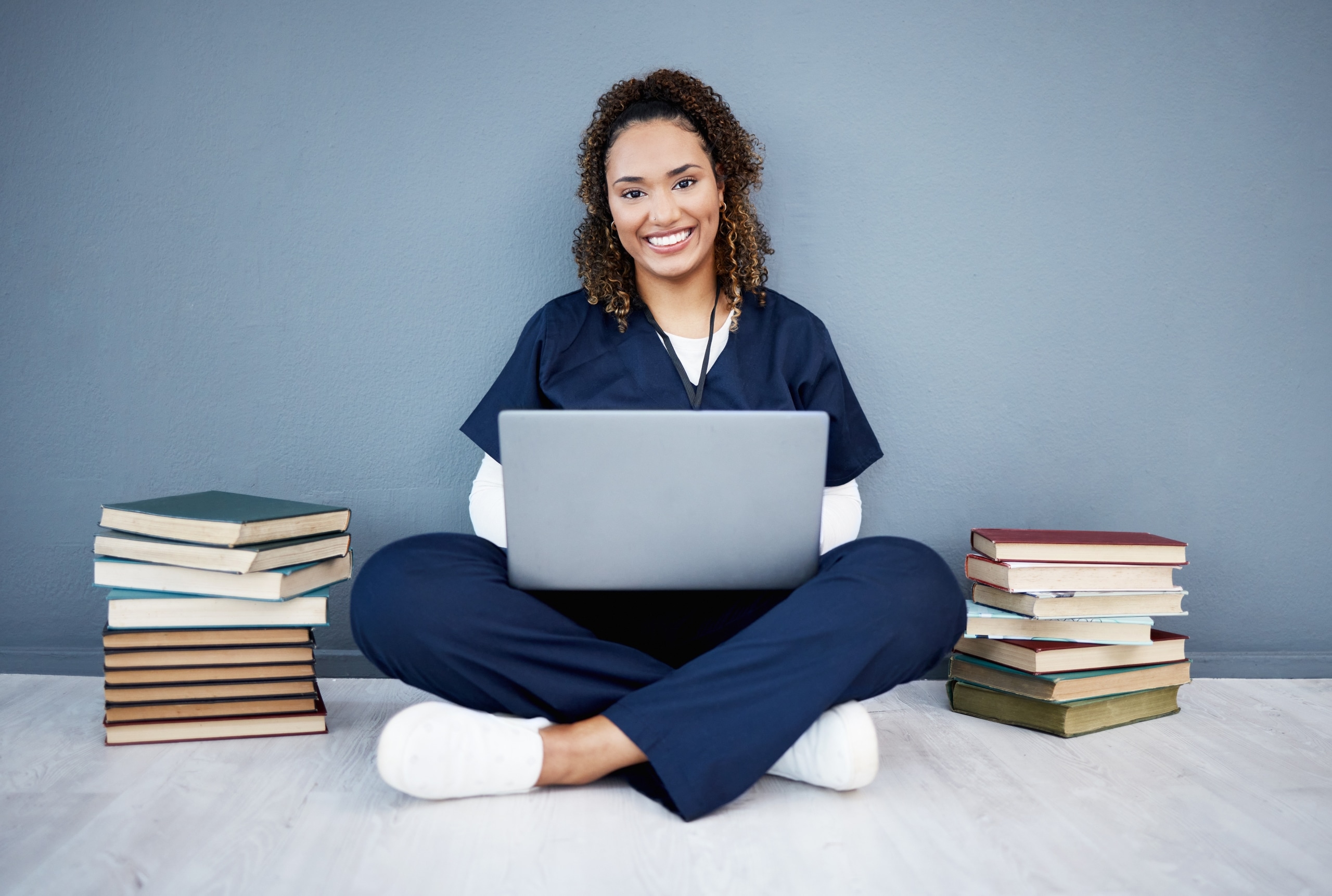 Smiling nurse with a laptop sitting near stacks of books