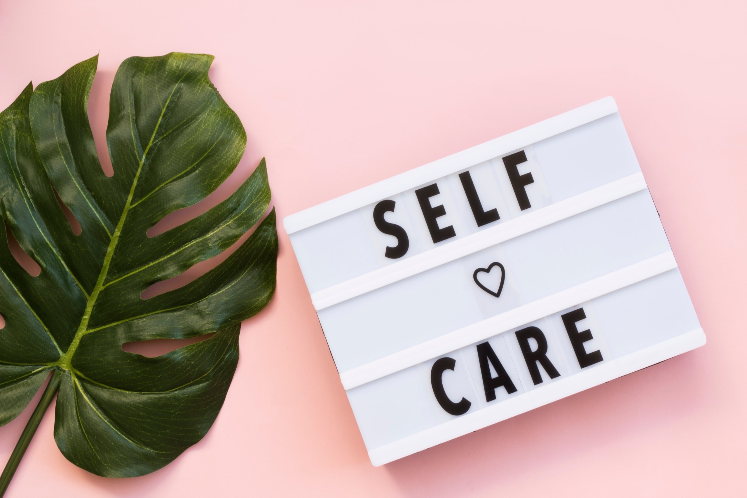 Sign that says self care against a pink backdrop