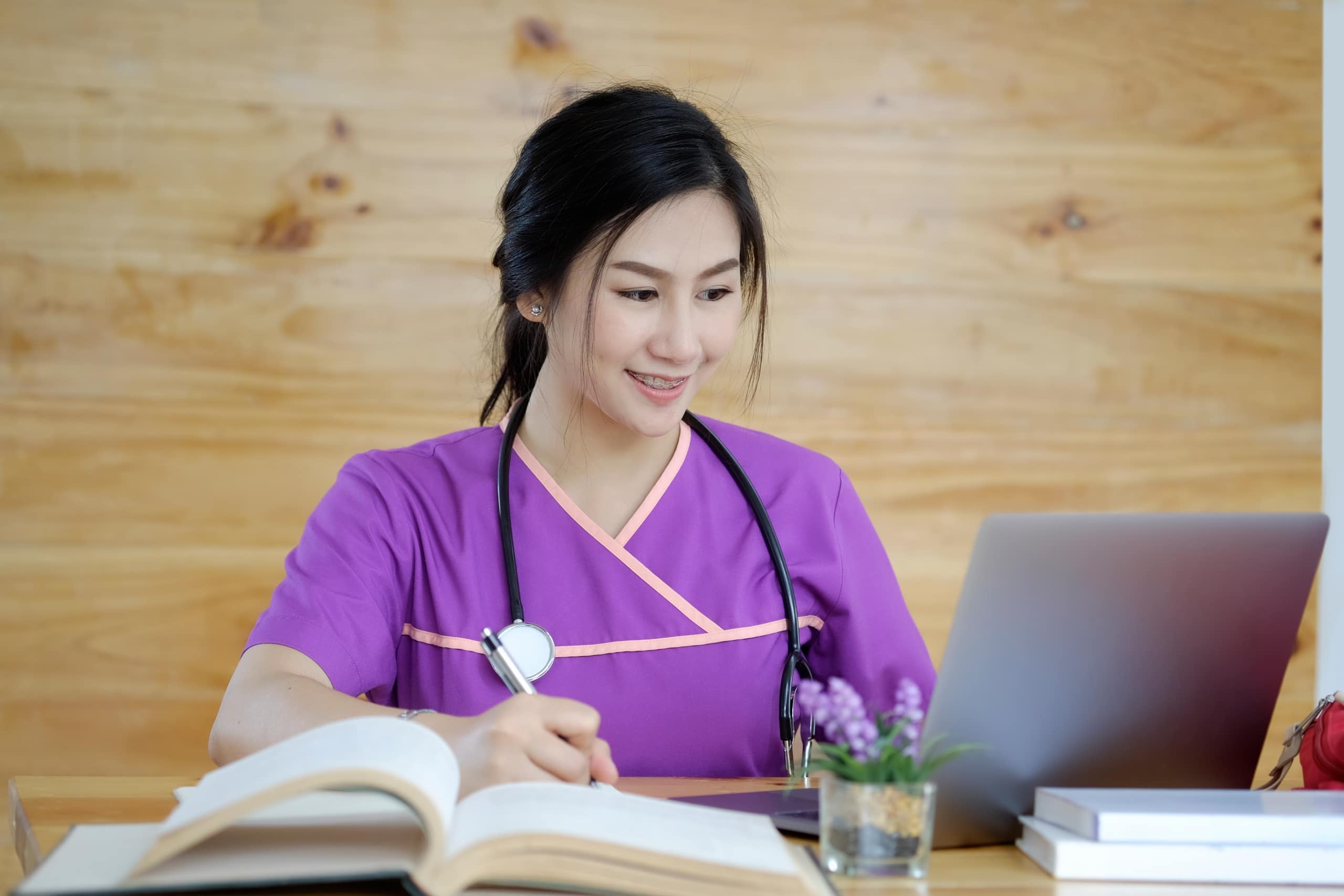 Asian nurse in purple scrubs using a laptop