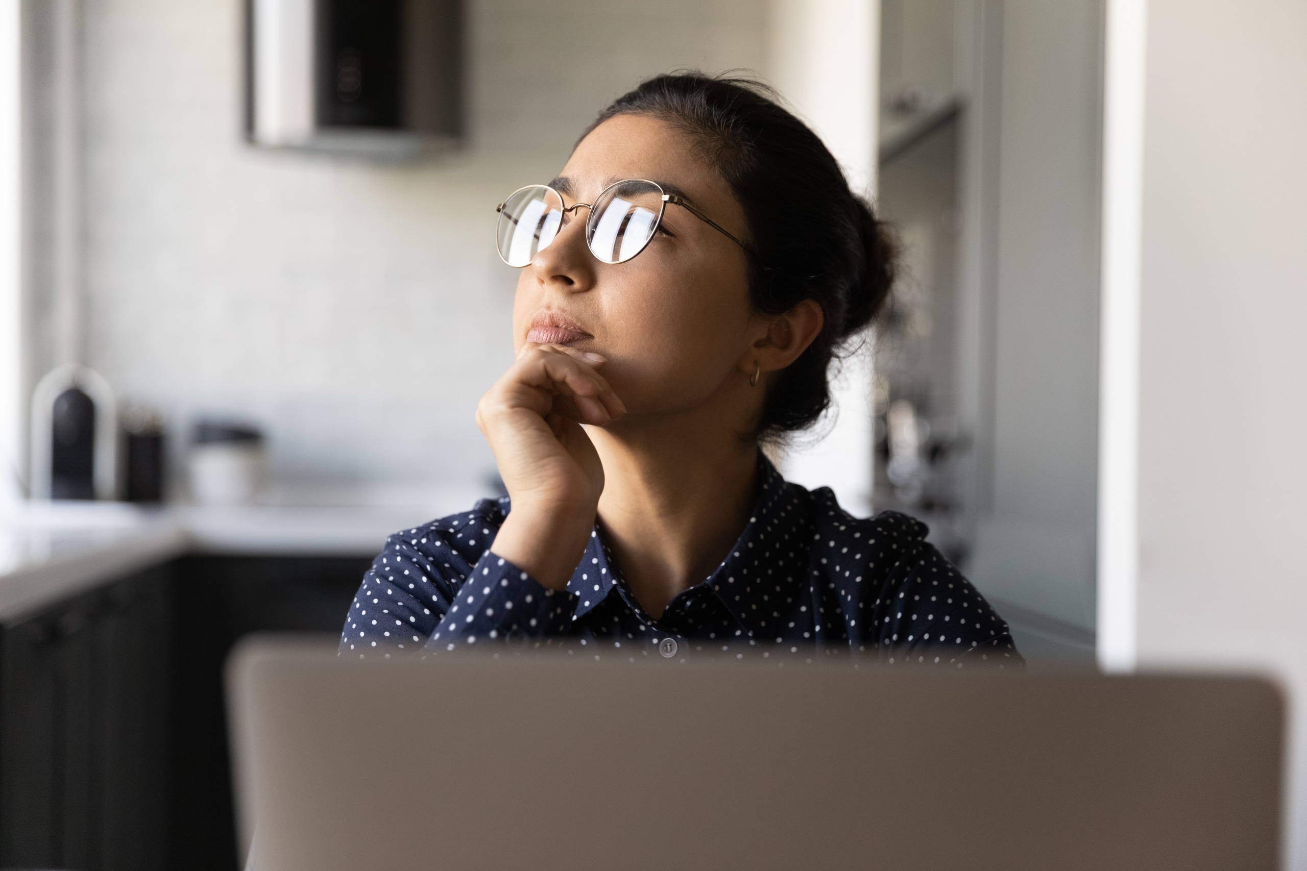 Woman in glasses at a desk deep in thought