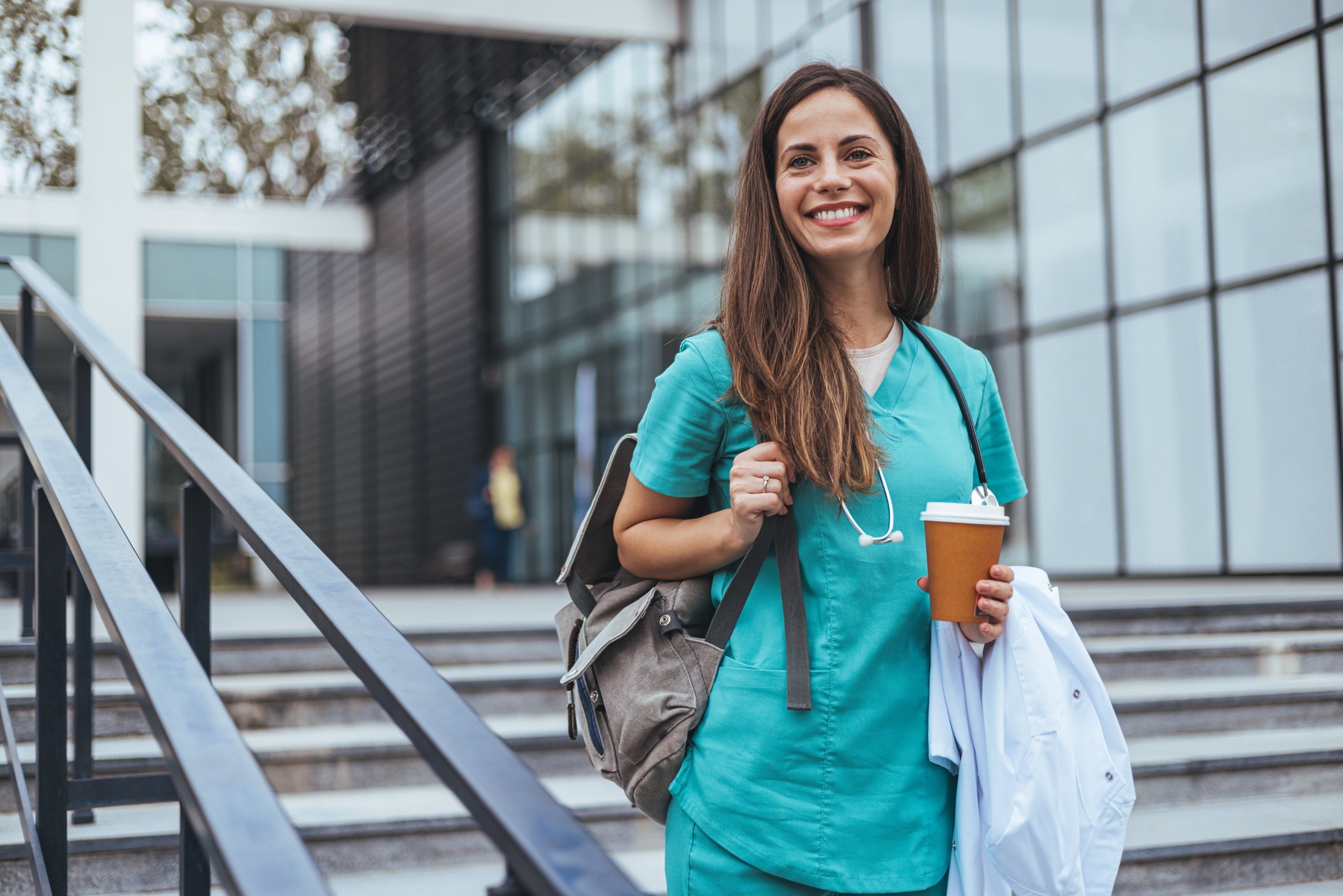 Female nurse standing outside with a backpack and coffee