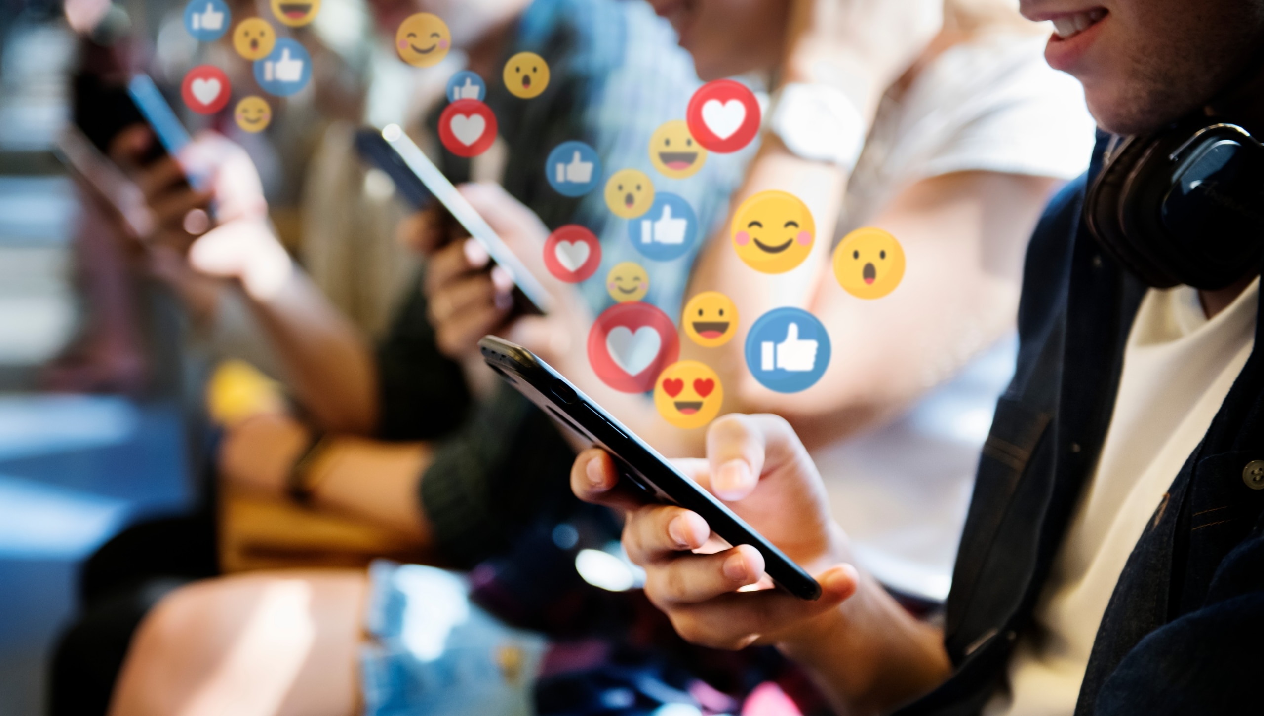 People using their mobile phones with social media symbols floating above them