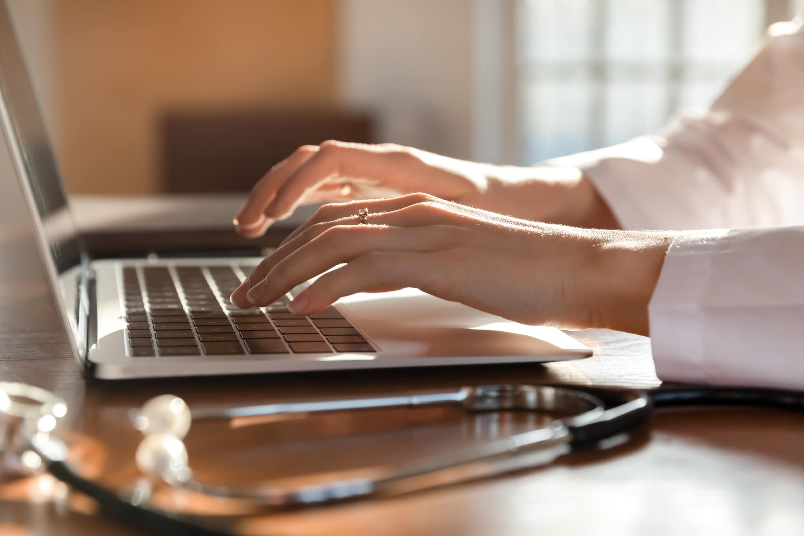 Close up of a woman typing on a laptop next to a stethoscope