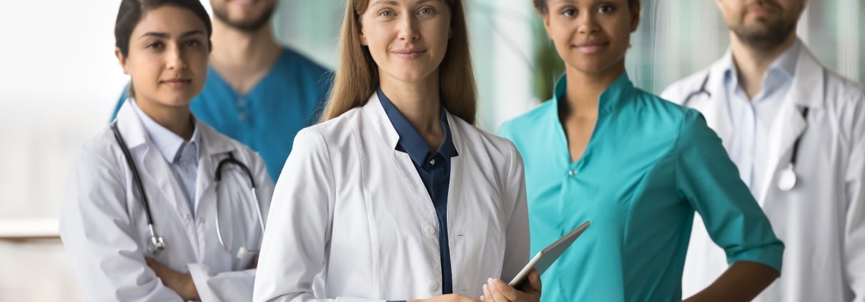 Smiling group of medical professionals wearing scrubs and white coats