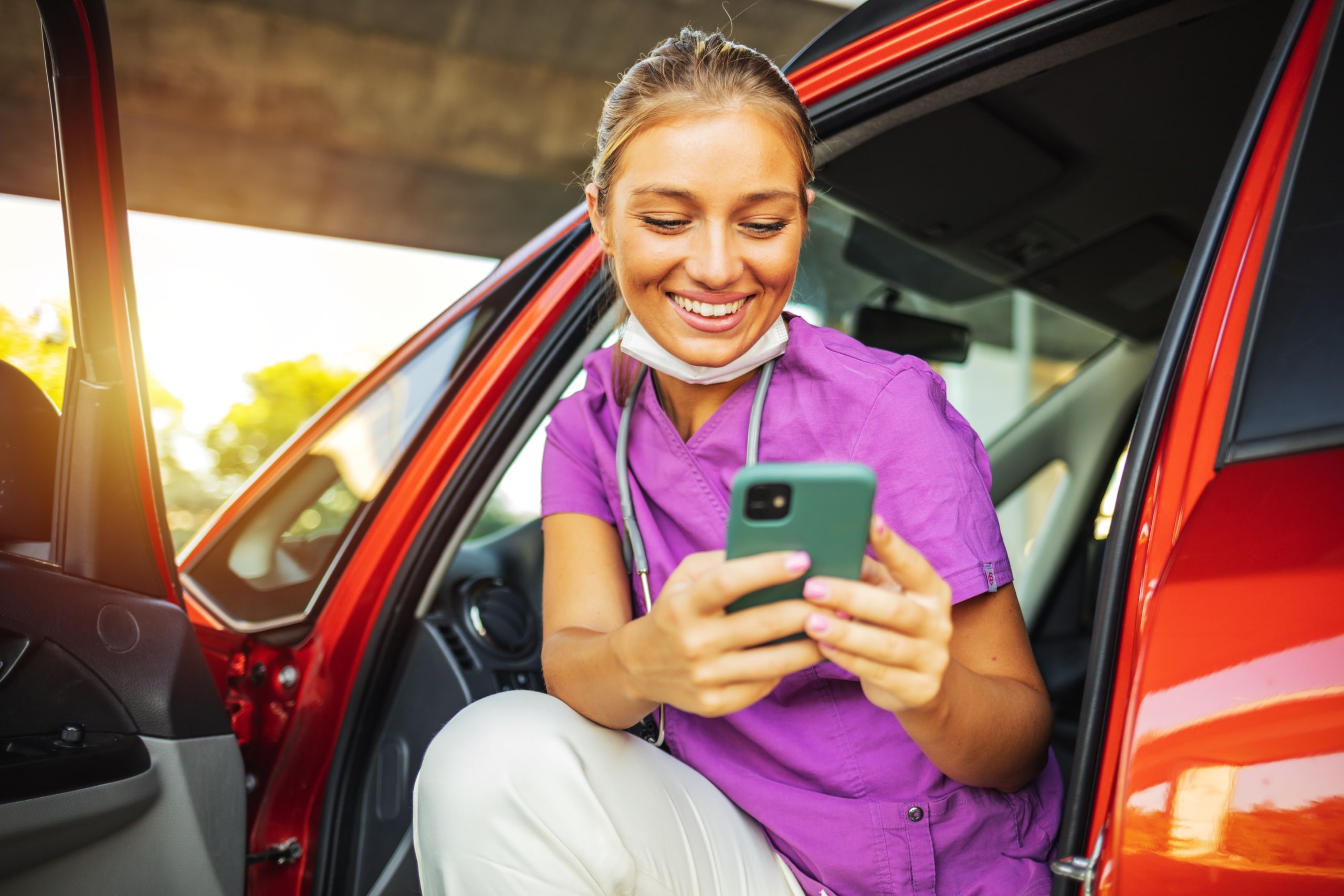 Smiling medical professional using their smart phone in a car