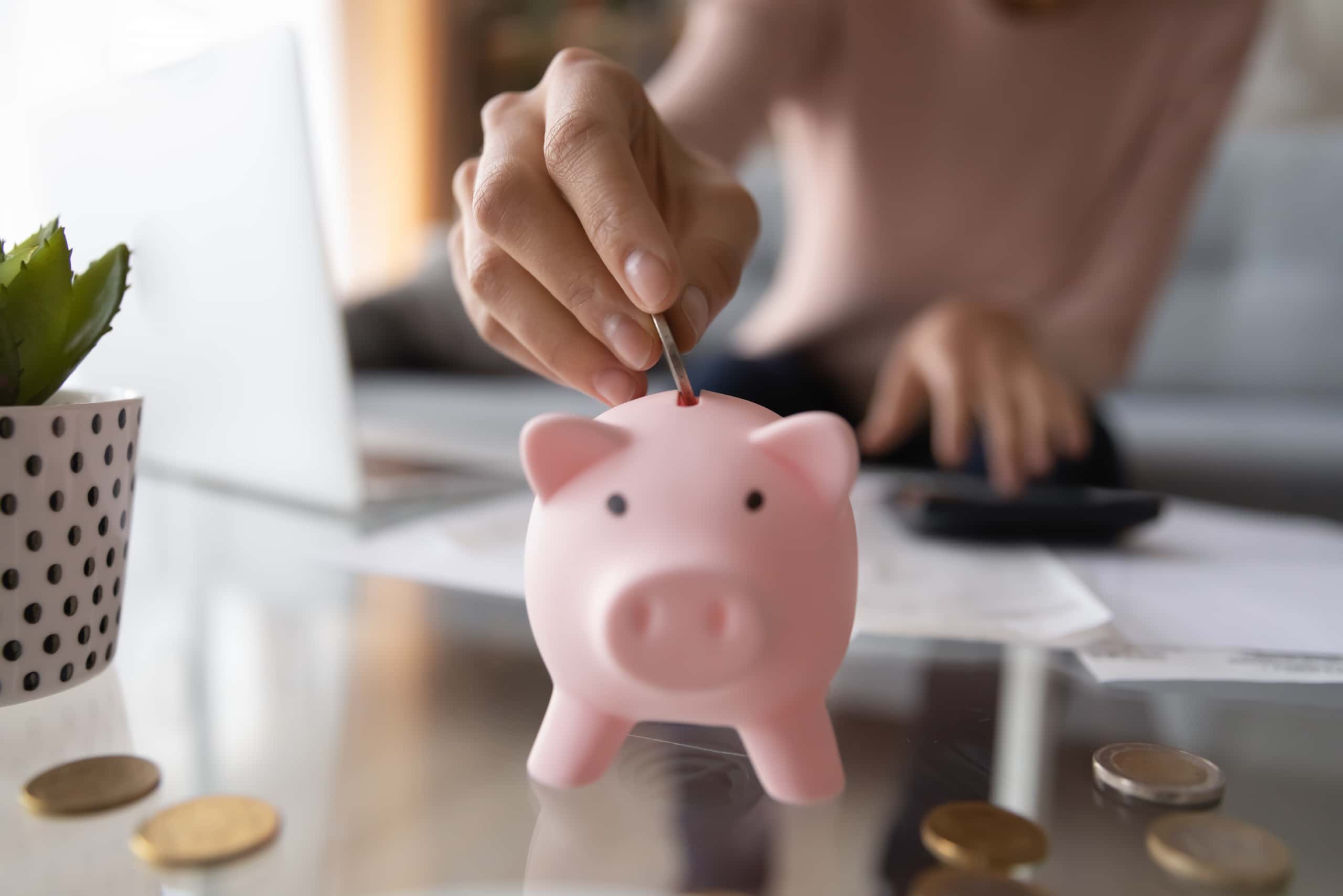 Close up of a woman placing coins in a piggy bank for her salary