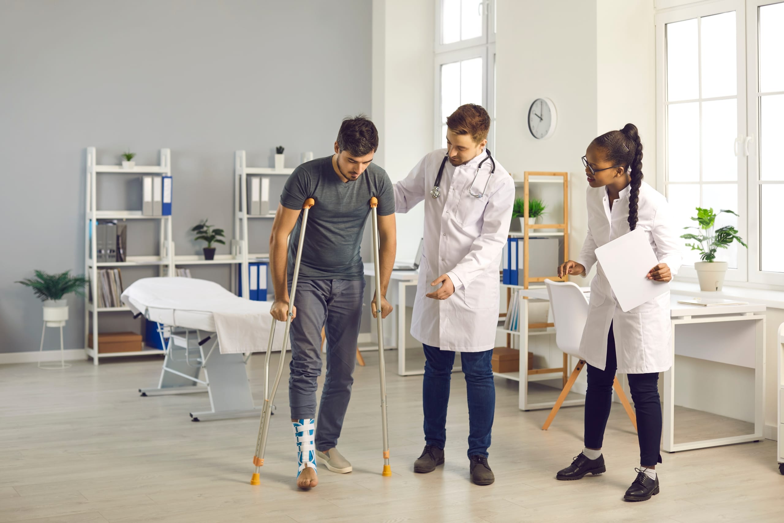 Group of medical professionals helping a male patient use crutches