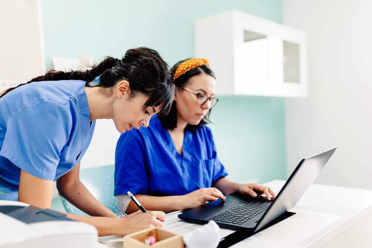 Two female nurses using a laptop and completing paperwork